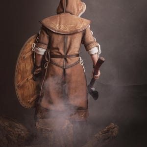Peut inclure: Costume en cuir marron avec capuche, bouclier et hache. Le costume pr&eacute;sente des coutures d&eacute;coratives et une capuche doubl&eacute;e de fourrure. Le bouclier est rond et en bois. La hache a un manche en bois et une lame en m&eacute;tal.