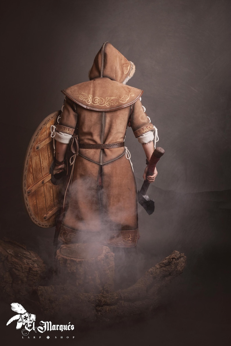 Peut inclure: Costume en cuir marron avec capuche, bouclier et hache. Le costume pr&eacute;sente des coutures d&eacute;coratives et une capuche doubl&eacute;e de fourrure. Le bouclier est rond et en bois. La hache a un manche en bois et une lame en m&eacute;tal.