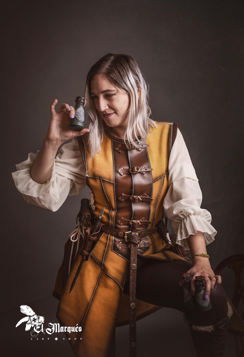 Peut inclure: Une personne porte un gilet en cuir jaune et marron avec une ceinture et un pantalon assortis. Le gilet a des boucles et des coutures d&eacute;coratives. La personne tient une petite bouteille de couleur fonc&eacute;e. L'image est sur fond gris fonc&eacute;.
