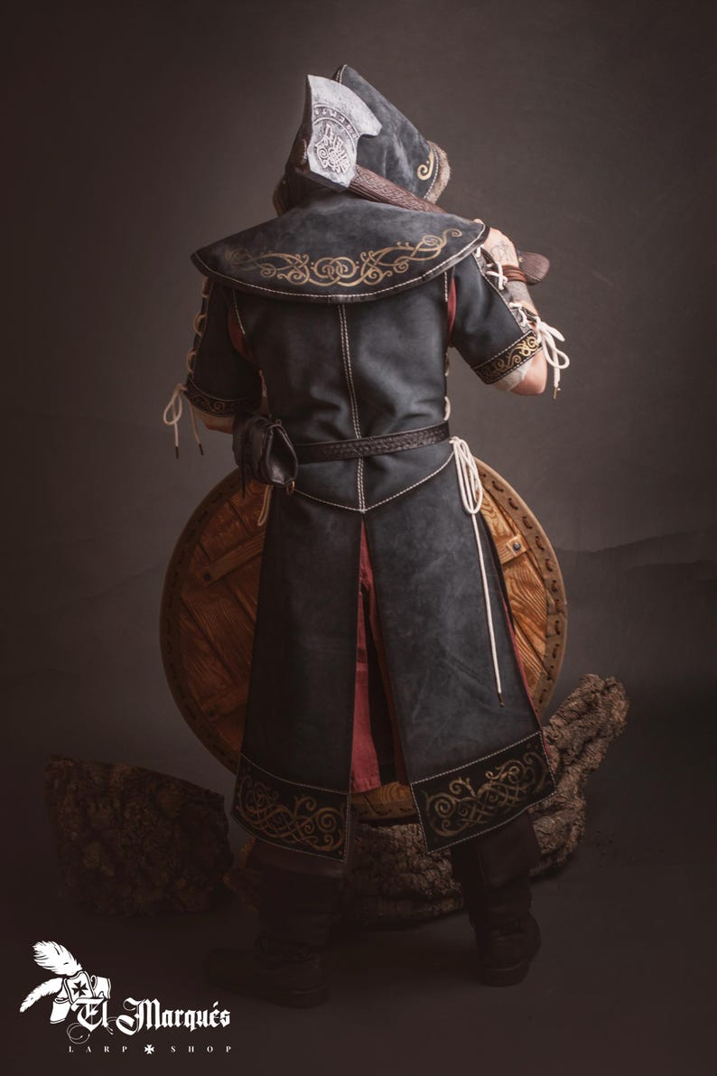 Peut inclure: Costume m&eacute;di&eacute;val avec une cape noire &agrave; capuche, broderies dor&eacute;es et ceinture en cuir. L'ensemble comprend un bouclier en bois et une hache. Id&eacute;al pour le cosplay ou les reconstitutions historiques.