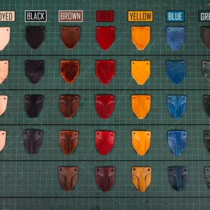May include: Leather samples in various colors and finishes, including undyed, black, brown, red, yellow, blue, and green. The samples are arranged in a grid with three rows and seven columns. Each row represents a different finish: smooth, textured, and shaped. The samples are all in the shape of a shield.