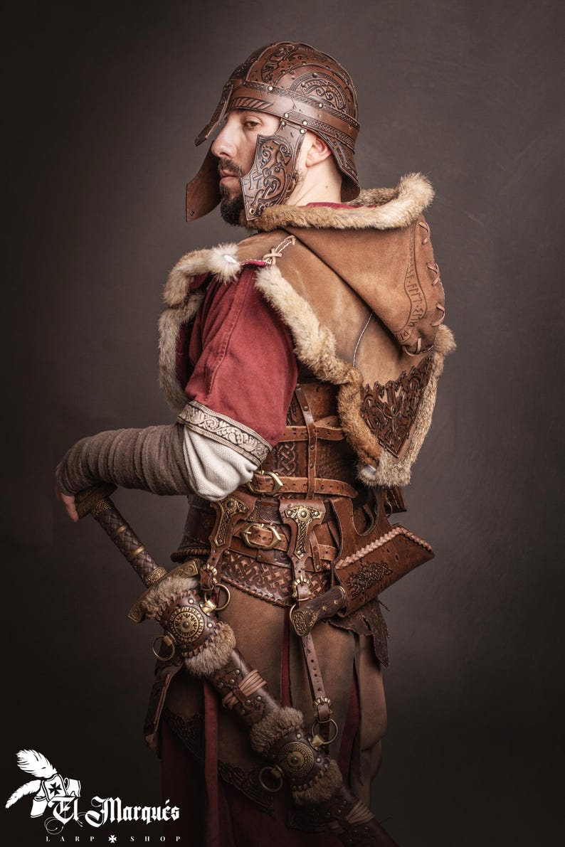 K&ouml;nnte beinhalten: Braunes Leder-Wikinger-Kriegerkost&uuml;m mit Helm, fellgef&uuml;ttertem Umhang und detailliertem G&uuml;rtel. Das Kost&uuml;m beinhaltet ein Schwert und eine Scheide, die ein historisches und Fantasy-Thema zeigen. Das Bild zeigt das Logo "El Marqu&eacute;s LARP Shop".
