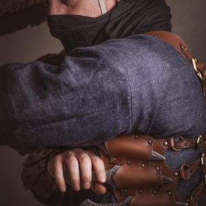 May include: A person wearing a dark blue robe and a wide-brimmed straw hat, holding a silver dagger with a leather sheath. The dagger is attached to a brown leather belt with metal accents.