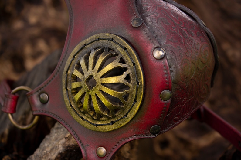 May include: A red leather mask with a gold metal design. The mask has a decorative floral pattern and is secured with metal rivets.