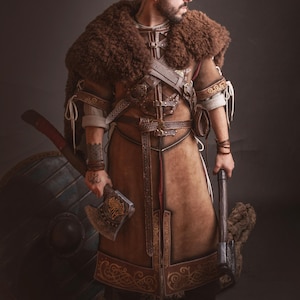 Peut inclure: Costume de Viking en cuir marron avec garniture en fourrure, d&eacute;tails complexes et ceinture d&eacute;corative. L'ensemble comprend une hache, un bouclier et un marteau. Le logo "El Marqu&eacute;s Larp Shop" est visible.
