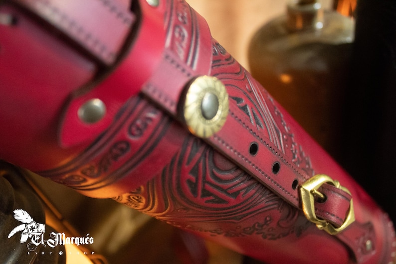 Peut inclure: Un carquois en cuir rouge avec des motifs en relief complexes et une boucle en laiton. Le carquois est dot&eacute; d'une sangle avec un bouton d&eacute;coratif en laiton.