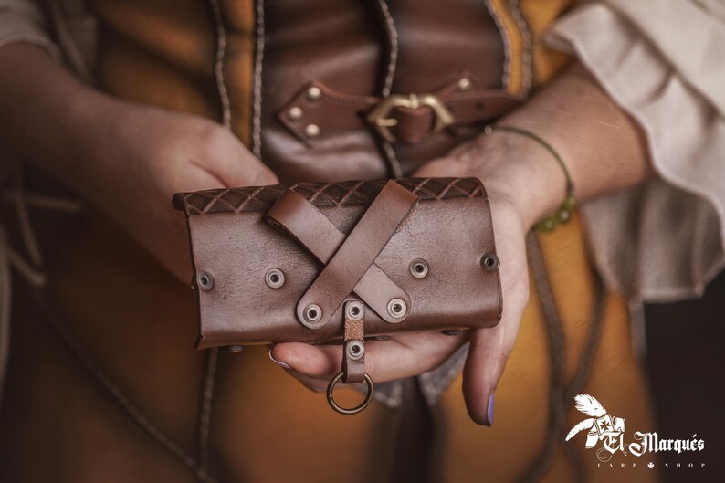 Peut inclure: Un bracelet de poignet en cuir marron avec un dessus &agrave; motif de losanges et des accents rivet&eacute;s. Le bracelet comporte une conception &agrave; lani&egrave;res crois&eacute;es et un anneau en m&eacute;tal. L'image montre le bracelet tenu.