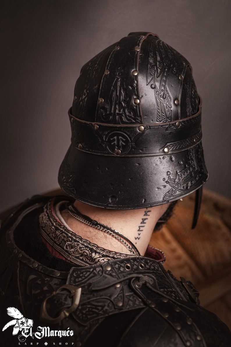 K&ouml;nnte beinhalten: Schwarzer Lederhelm mit gepr&auml;gten Designs und Messingnieten. Der Helm hat einen Nackenschutz und ein dekoratives Band. Das Bild zeigt die R&uuml;ckseite des Helms und einen Teil der R&uuml;stung des Tr&auml;gers. Der Helm ist von einem LARP-Shop.