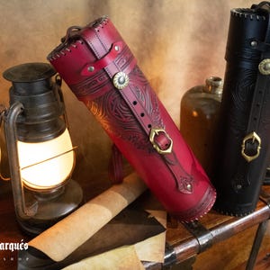Peut inclure: Deux tubes en cuir avec des motifs en relief complexes et des accents en laiton. Les tubes reposent sur une surface en bois avec un morceau de papier roul&eacute; et une lanterne.