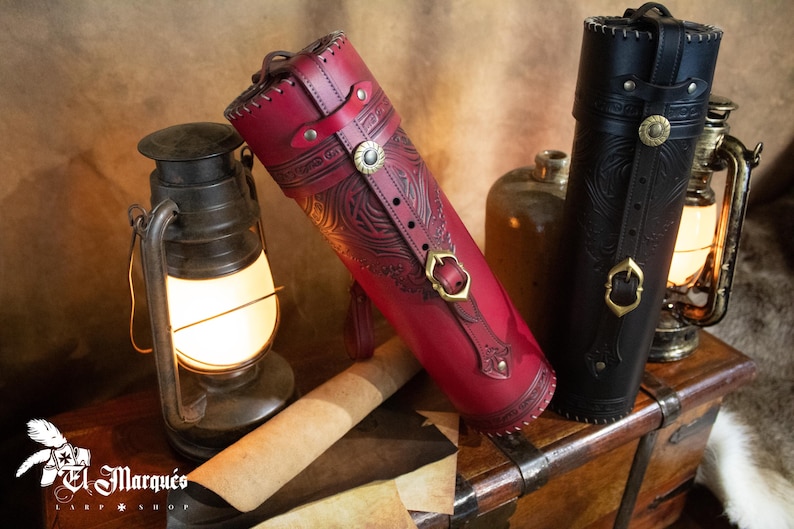 Peut inclure: Deux tubes en cuir avec des motifs en relief complexes et des accents en laiton. Les tubes reposent sur une surface en bois avec un morceau de papier roul&eacute; et une lanterne.