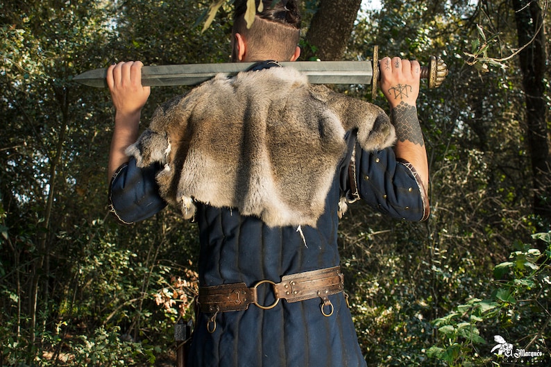 May include: A person wearing a blue tunic with a fur collar and a leather belt with metal accents. They are holding a sword over their shoulder.