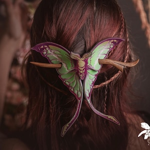 Könnte beinhalten: Haarschmuck mit einem Schmetterlingsdesign in Grün, Lila und Gelb. Der Schmetterling wird mit einem Holzstab befestigt, wodurch eine einzigartige Haarspange entsteht. Rötliches Haar im Hintergrund.