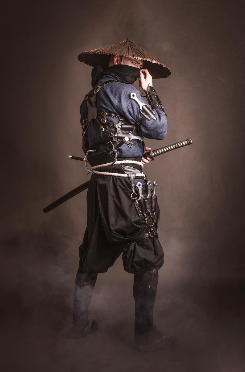 May include: A person wearing a blue and black outfit with a wide-brimmed hat, holding a sword and a variety of knives. The person is standing in a smoky environment.