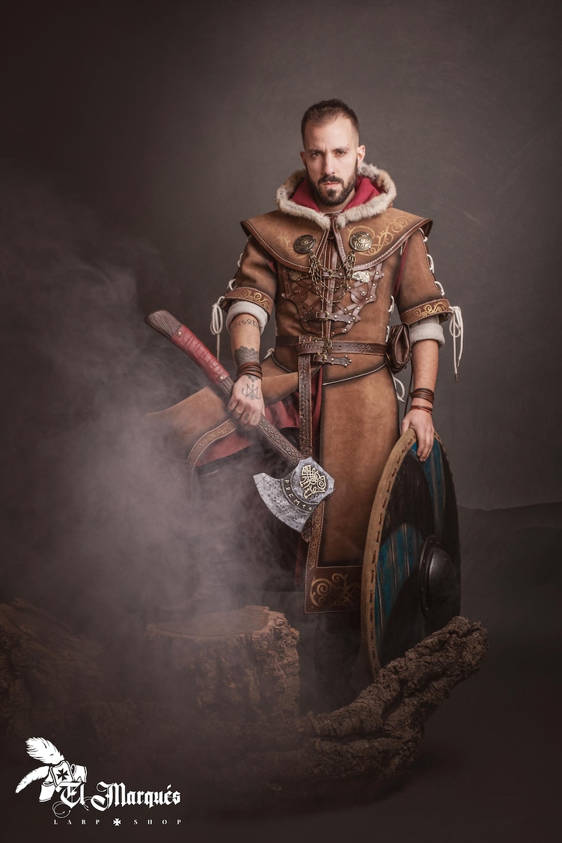 Peut inclure: Une personne porte un costume de Viking en cuir marron, tenant une hache de guerre et un bouclier rond. Le costume comprend une capuche doubl&eacute;e de fourrure et des d&eacute;tails complexes. La hache a une t&ecirc;te argent&eacute;e et un manche rouge. Le bouclier est marron et bleu.