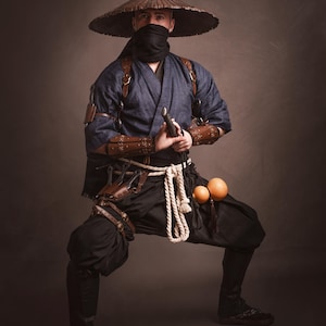 May include: A person wearing a blue and brown costume with a wide-brimmed hat, holding a sword and standing in a fighting pose.