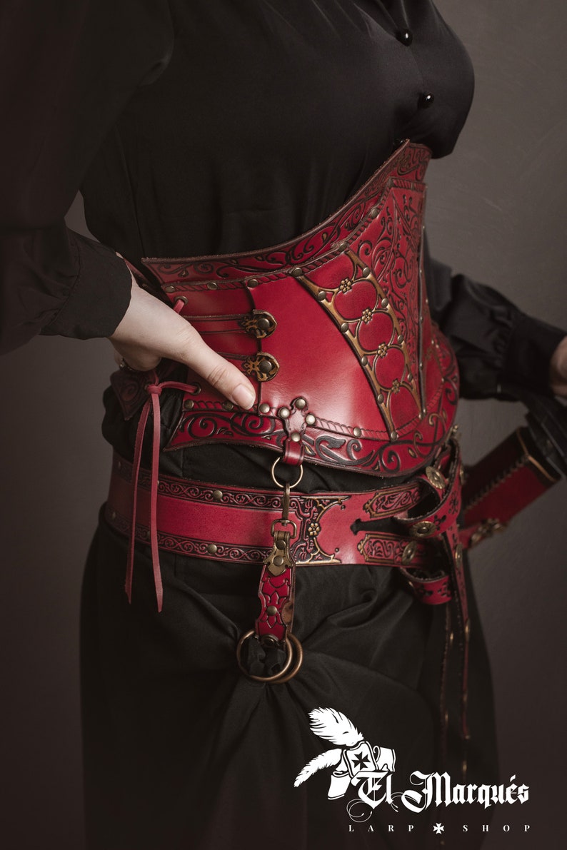 K&ouml;nnte beinhalten: Ein rotes Lederkorsett mit aufwendigen floralen Mustern und Metallverzierungen. Das Korsett wird &uuml;ber einem schwarzen Hemd getragen und mit einem passenden roten Lederg&uuml;rtel und einer Schwertscheide kombiniert.