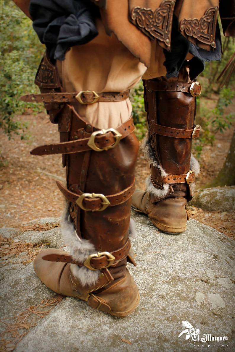 May include: Brown leather leg armor with fur trim and multiple buckles. The armor is worn on both legs and has a distressed look.