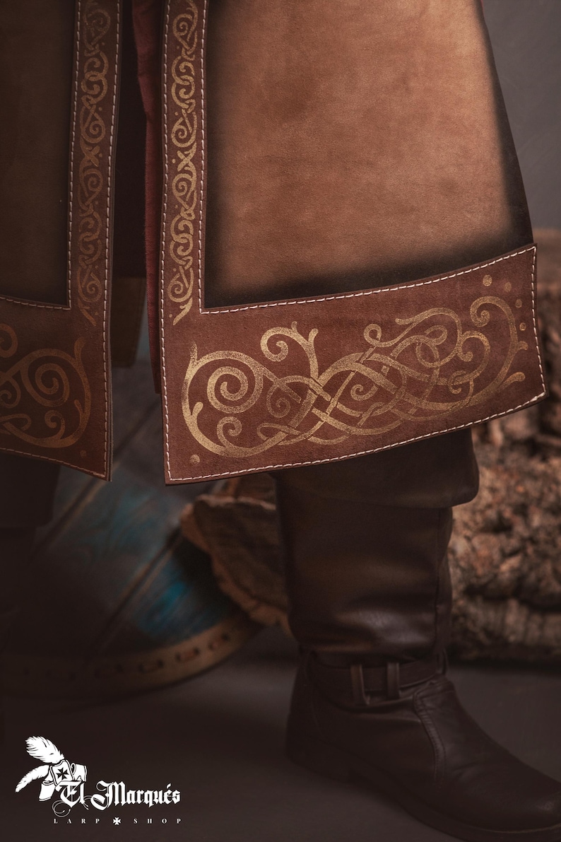 Peut inclure: Gros plan sur un v&ecirc;tement en cuir marron avec une bordure dor&eacute;e orn&eacute;e de n&oelig;uds celtiques. Le v&ecirc;tement semble faire partie d'un costume, avec des coutures visibles et une botte en cuir marron fonc&eacute;. L'image a une tonalit&eacute; chaude et terreuse.