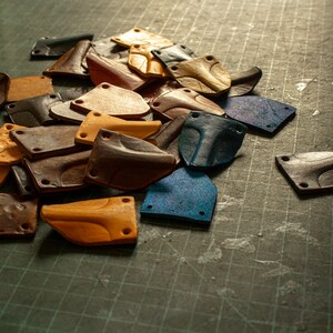 May include: A collection of leather pieces in various colors and shapes, including brown, tan, blue, and gray. The pieces are arranged on a green surface.