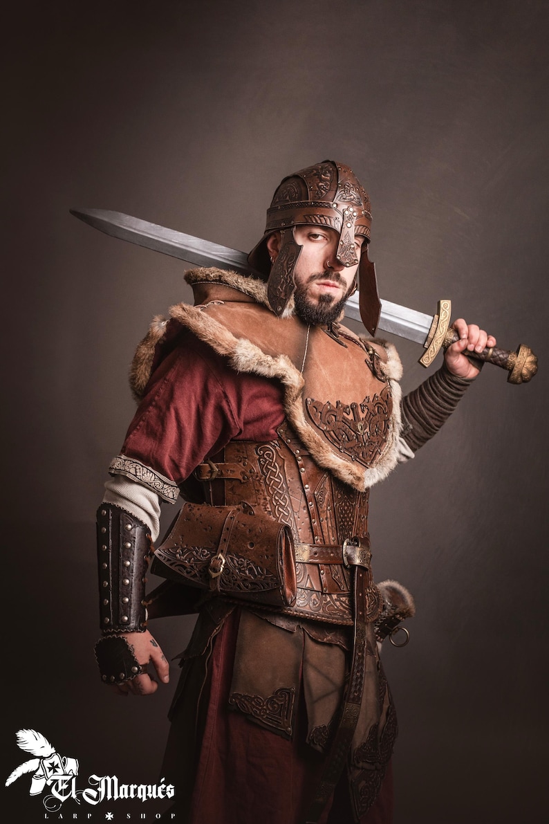 K&ouml;nnte beinhalten: Ein Krieger in brauner Lederr&uuml;stung, einem passenden Helm und einem pelzgef&uuml;tterten Umhang, der ein gro&szlig;es Schwert h&auml;lt. Die R&uuml;stung weist aufwendige gepr&auml;gte Designs auf. Der Krieger tr&auml;gt ein rotes Hemd unter der R&uuml;stung.