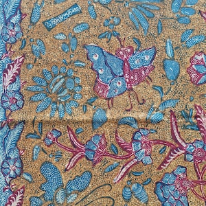 Könnte beinhalten: Detaillierter Stoff mit braunem Hintergrund, der ein sich wiederholendes Muster aus blauen und kastanienroten Blumen, Blättern und einem Schmetterling aufweist. Das Design enthält ein kleines rechteckiges Textelement. Die Gesamtästhetik erinnert an Batik.