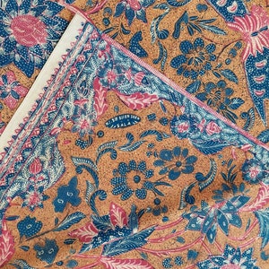 Könnte beinhalten: Ein brauner Stoff mit einem blauen und rosa floralen Muster. Der Stoff hat einen weißen Rand und den Text "NI SIR DIEN SOEN SALA" in der Mitte.
