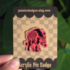 May include: A pink and black acrylic pin badge featuring a hyena design with star accents. The pin is on a brown and tan checkered background with the text "Acrylic Pin Badge". The Etsy shop URL is visible.