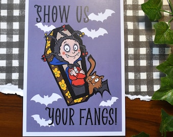 May include: A rectangular greeting card with a light purple background featuring a cartoon vampire with dark hair in a coffin decorated with yellow flowers. The text reads SHOW US YOUR FANGS! with white bat silhouettes and a small brown winged creature.