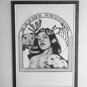 May include: Black and white framed art print featuring a woman with long hair and two seals. The artwork includes text in an arch above the woman. The frame is dark brown.