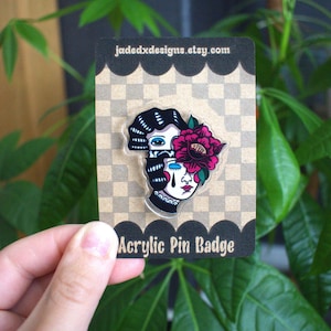 May include: Acrylic pin badge featuring a split face design with a flower. The pin has a black and white color scheme with a pink flower. The text "Acrylic Pin Badge" is at the bottom of the card.