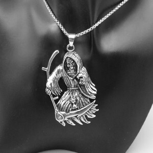 May include: A silver necklace featuring a detailed pendant of the Grim Reaper holding a scythe. The pendant is on a silver chain.