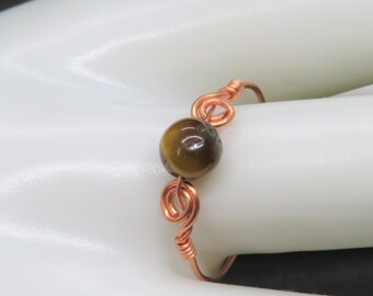 May include: A copper wire ring with a brown tiger's eye gemstone.