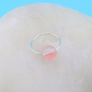 May include: A silver ring with a pink and white gemstone. The ring is sitting on a white rock.