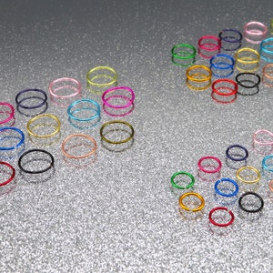 May include: Assortment of colourful metal rings, some are stacked, others are scattered on a silver sparkly surface.