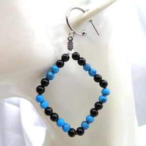 May include: A single earring featuring a silver hoop and a diamond-shaped pendant. The pendant is crafted from alternating black and turquoise beads. The earring is designed for ear wear.