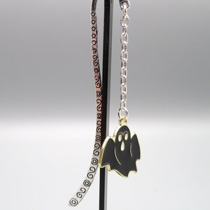 May include: Silver bookmark with a black ghost charm hanging from a silver chain. The bookmark has a decorative pattern of swirls.