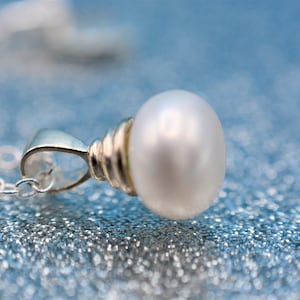 以下が含まれることがあります： 白い真珠のペンダントが付いたシルバーチェーンネックレス。真珠はシルバーのベゼルにセットされており、チェーンは繊細です。