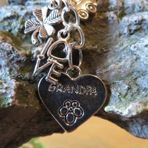 Puede incluir: Llavero de plata con abalorios, incluyendo un trébol de cuatro hojas, un corazón con la palabra "love" y un corazón con la palabra "grandpa".