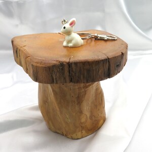 May include: A white ceramic rabbit keychain with a silver metal ring. The keychain is sitting on a wooden stump with a rough, natural surface.