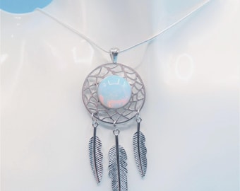 May include: A silver-toned necklace featuring a circular dreamcatcher pendant with a central iridescent cabochon stone. Three detailed silver-toned feather charms hang from the bottom of the circular frame, suspended on a thin silver-toned chain.