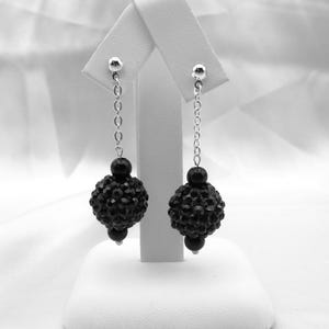 May include: A pair of black dangle earrings with a silver chain and a black crystal ball at the end.