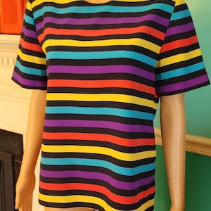 May include: A striped short-sleeved shirt with black, yellow, red, purple, and blue stripes. The shirt is on a mannequin.