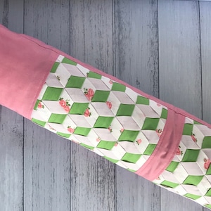May include: A pink and green fabric roll with a quilted pattern of white and green squares with pink roses. The fabric is folded in half and the edges are sewn together.