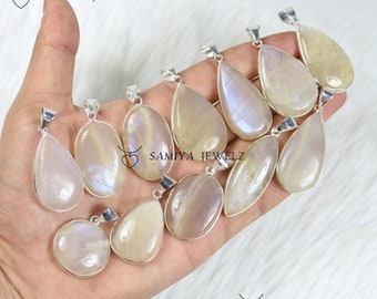 May include: A collection of iridescent moonstone pendants in various shapes, including teardrop and oval, with silver-colored metal settings. The pendants display a range of colors, from pale yellow to lavender, and are arranged on a white surface. The brand name "SAMIYA JEWELZ" is visible.