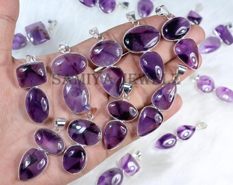 May include: A collection of amethyst pendants in various shapes, including oval, teardrop, and rectangular, with silver-colored metal settings. The pendants display a range of purple hues and are displayed on a white surface.