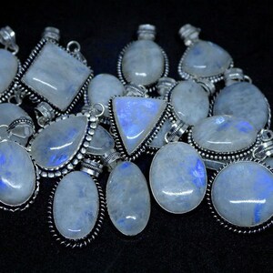 May include: A collection of silver pendants with moonstone gemstones. The pendants are oval, teardrop, and square shaped. The moonstone is a milky white color with a blue iridescent sheen.