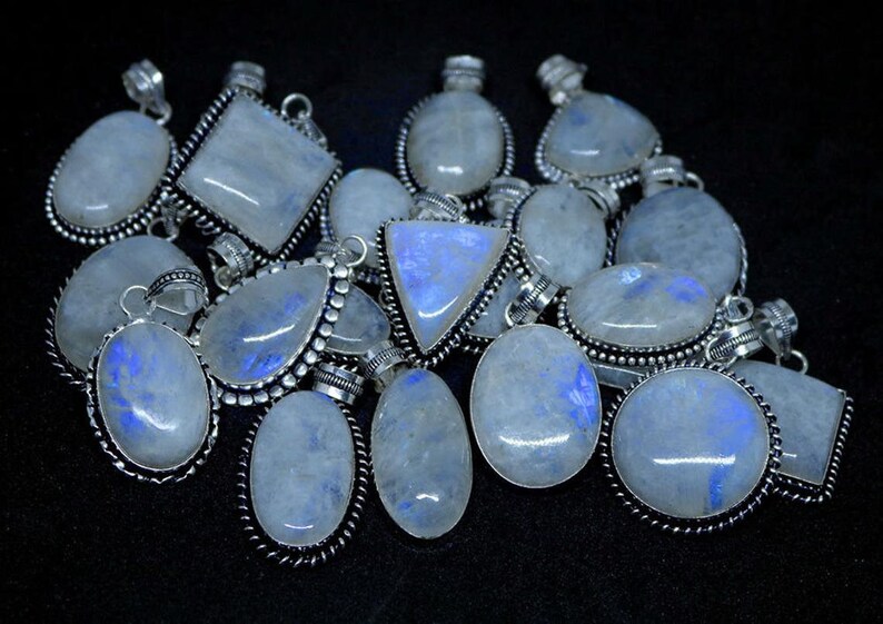 May include: A collection of silver pendants with moonstone gemstones. The pendants are oval, teardrop, and square shaped. The moonstone is a milky white color with a blue iridescent sheen.