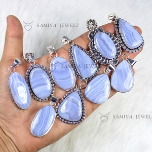 Puede incluir: Colección de colgantes de ágata de encaje azul en varias formas, incluyendo óvalos, lágrimas y triángulos. Cada colgante tiene una fianza plateada. Los colgantes se muestran sobre una superficie blanca, con el texto "SAMIYA JEWELZ" visible.