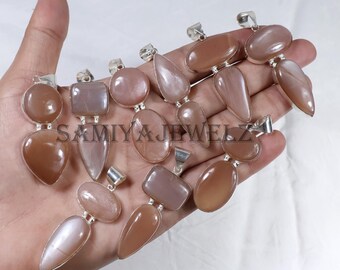 Puede incluir: Una colección de colgantes de piedras preciosas en varias formas, incluyendo ovaladas, de lágrima y rectangulares. Los colgantes son de color melocotón y beige, con colgantes de metal plateado. El texto "SAMIYA JEWELZ" es visible.