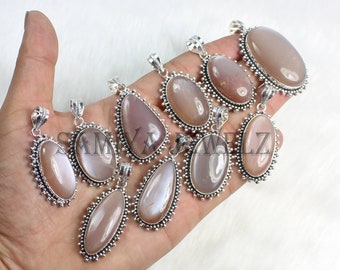 Puede incluir: Una colección de colgantes de piedras preciosas de color melocotón en varias formas, incluyendo ovaladas y de lágrima. Cada colgante presenta una piedra pulida engastada en un marco decorativo plateado. Los colgantes se muestran sobre un fondo blanco.